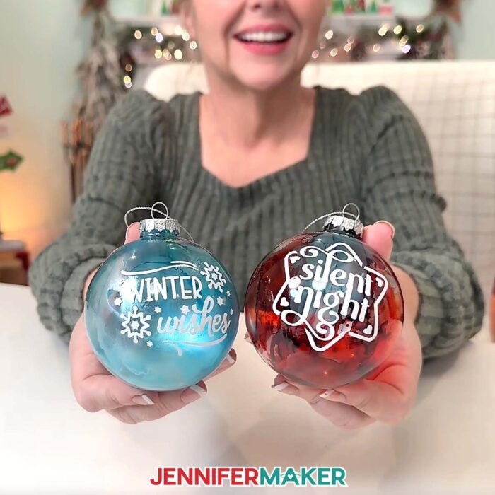 Jennifer shows off a blue ornament with a white "Winter Wishes" vinyl decal and a red ornament with a white "Silent Night" vinyl decal.