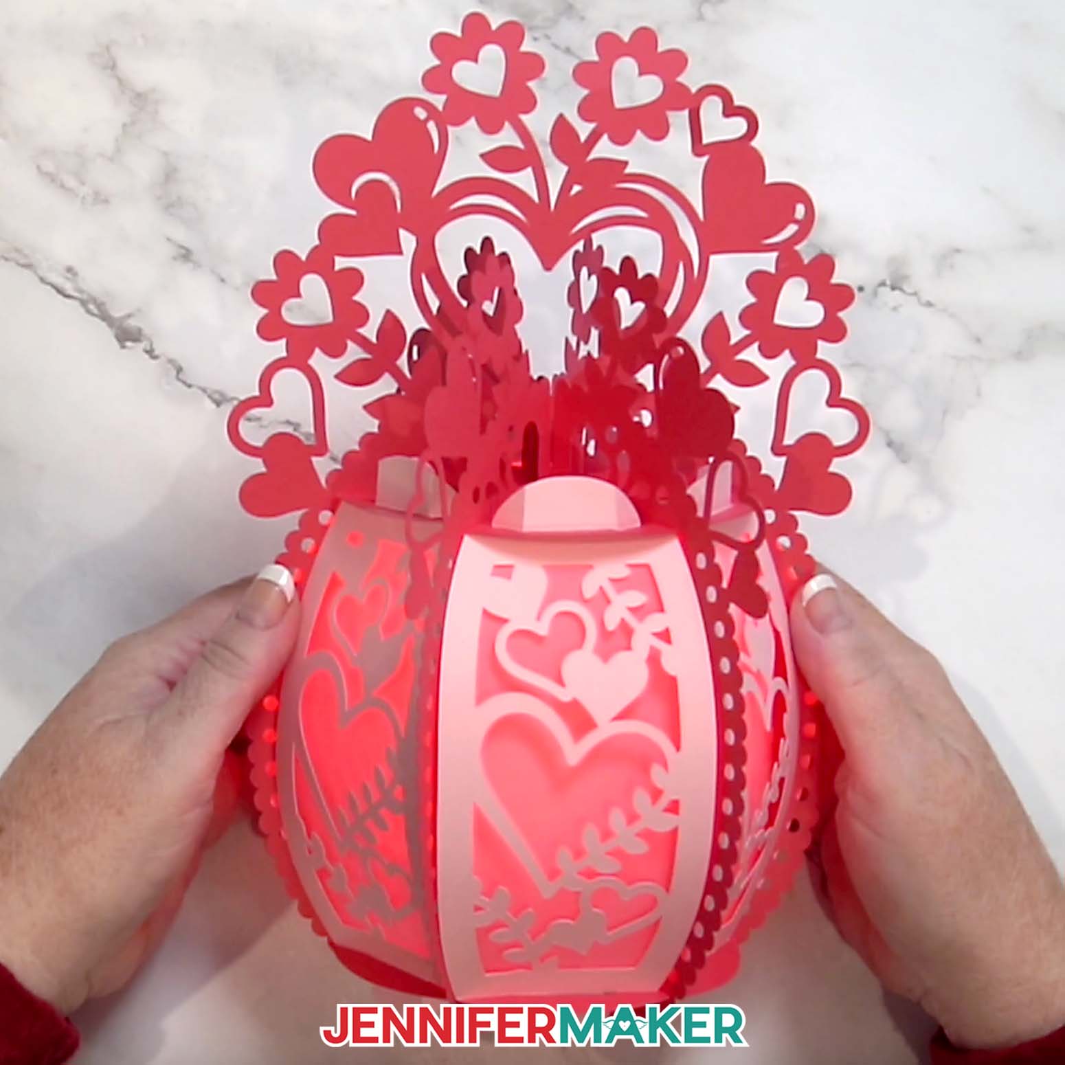 The finished 3D ornate paper lantern heart design made of red and pink cardstock with a light showing from the inside.