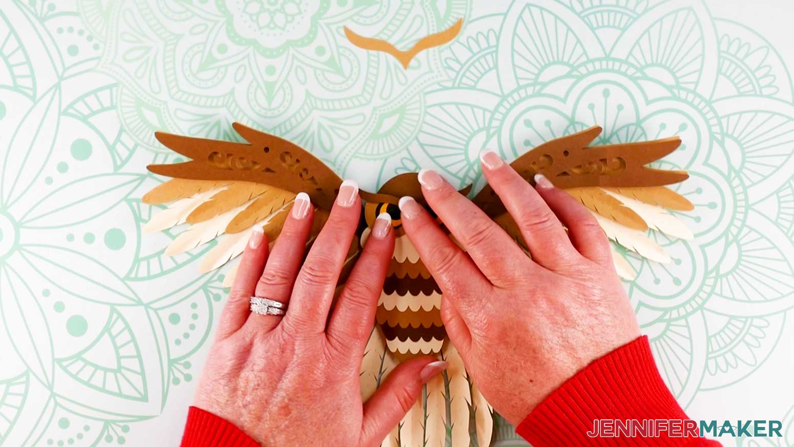 An overhead photo of two hands pressing down on the dark brown tuft piece to adhere it above the face piece on the assembled layered owl on the work surface