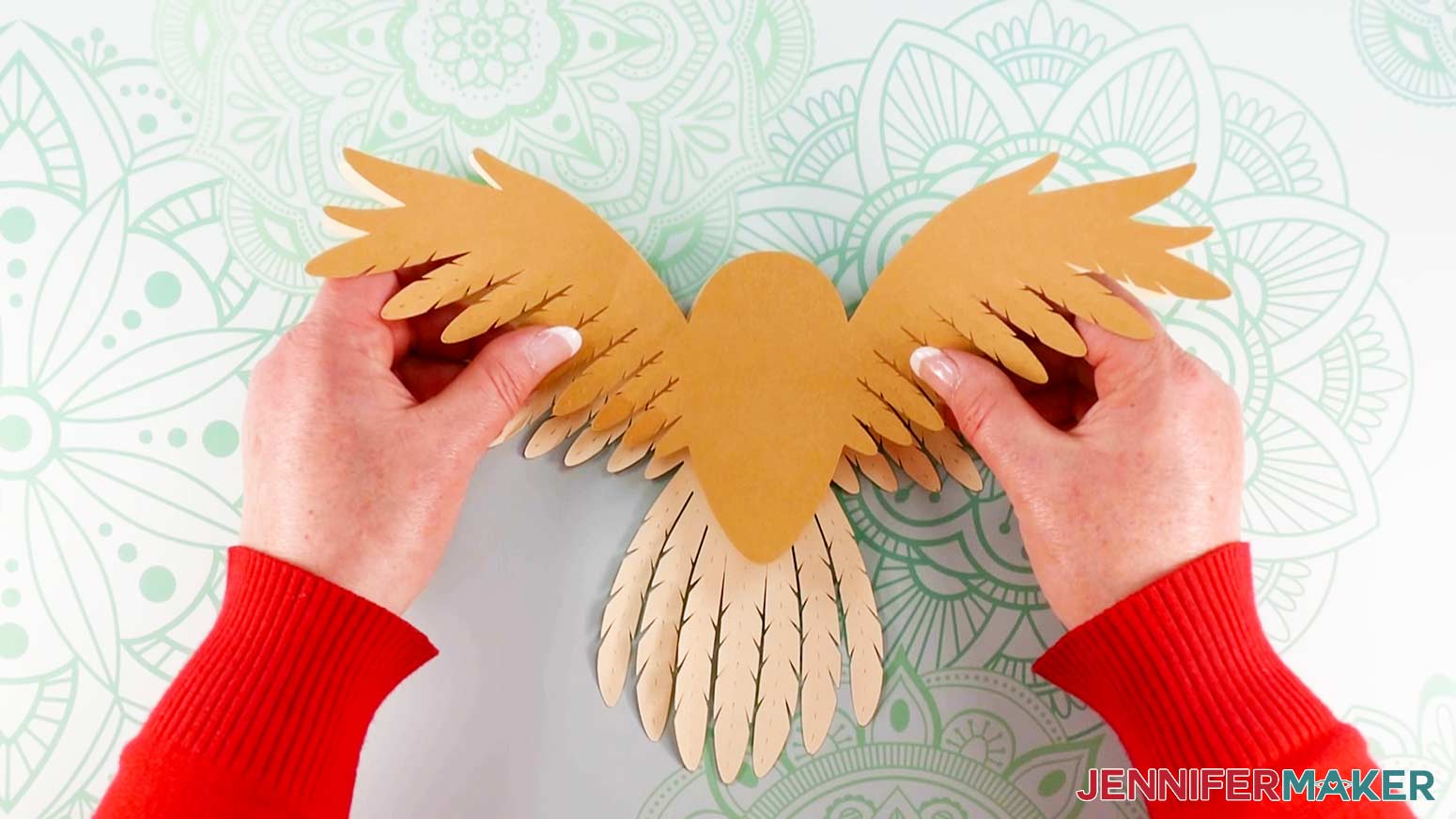 An overhead photo showing the middle wing layer of the layered owl being aligned and pressed down to the bottom wing layer on the work surface