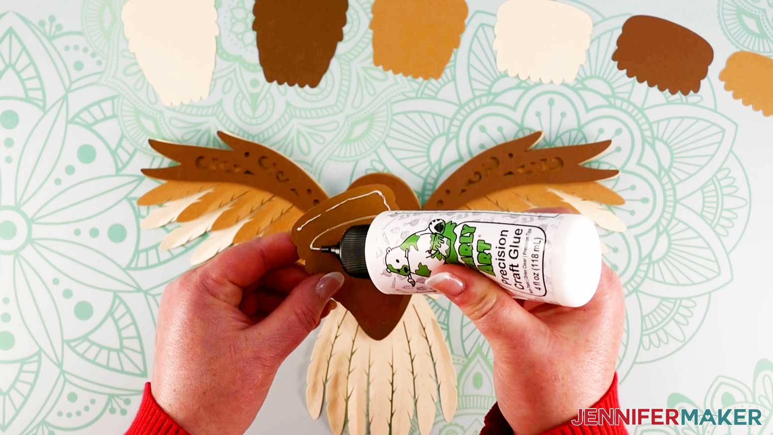 An overhead photo showing glue being applied to the back of the largest cardstock piece of the front feathers for the layered owl design