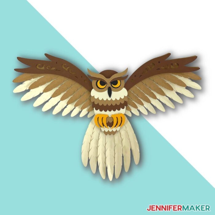 Papercraft layered owl svg made of tan, brown, and yellow cardstock with spread wings on a blue and white background