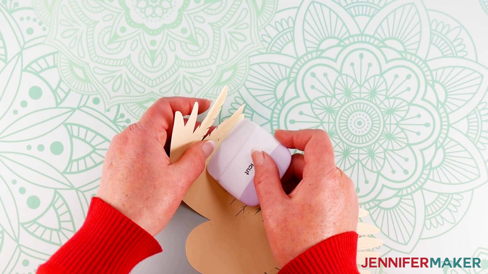 A photo showing a Cricut scraper tool held in one hand shaping a cardstock feather attached to a piece of the cut owl SVG design held in another hand