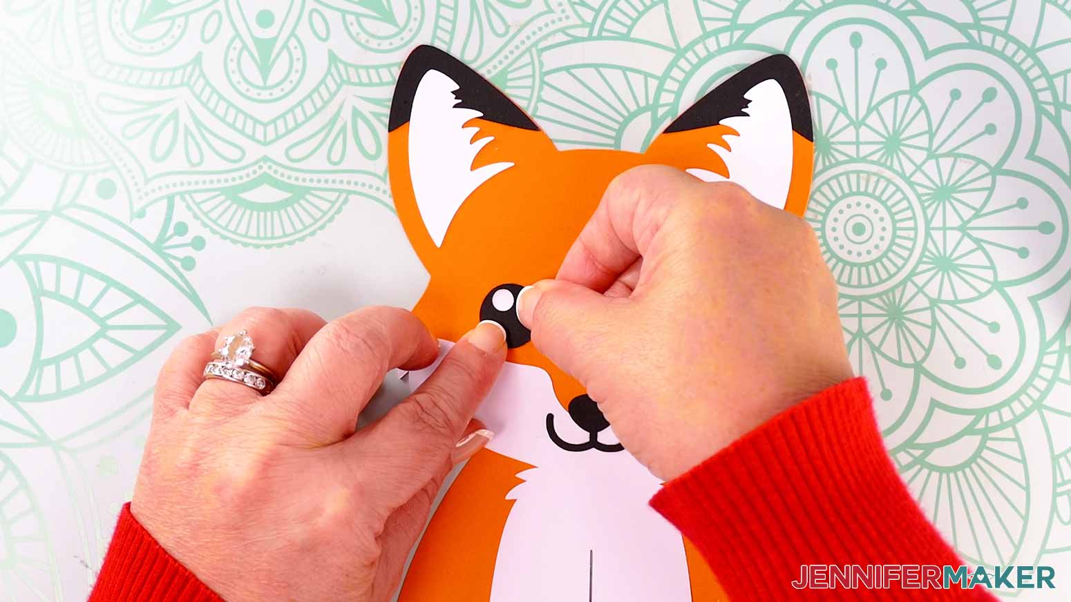 Adhere the black and white pieces of the fox lantern's left eye on the fox's face.