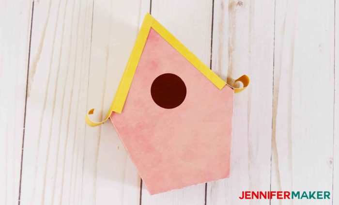 A finished pink paper birdhouse with a yellow rolled edge roof