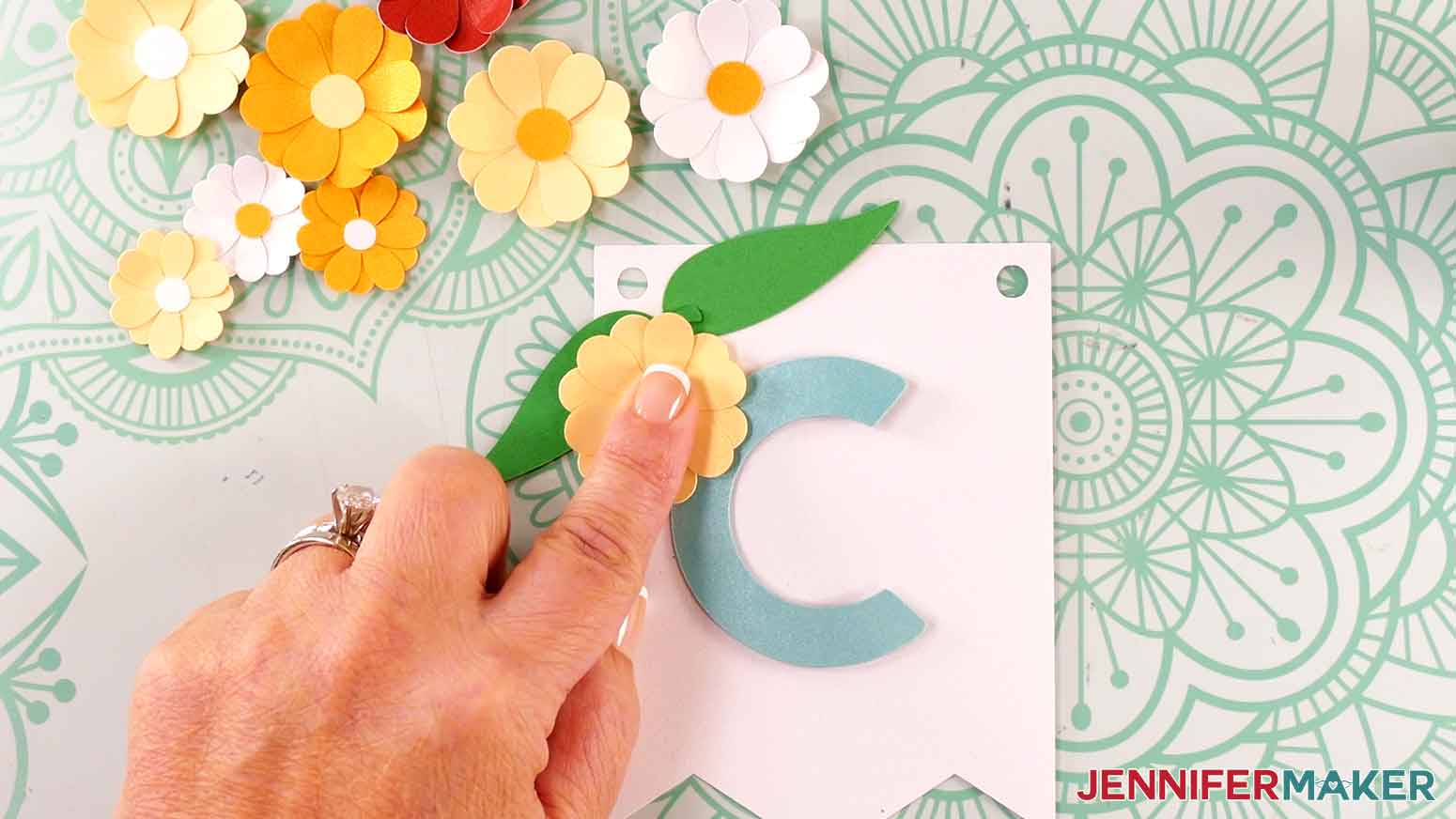 Apply glue to the back of the yellow flower and press it in to place over the upper left leaf.