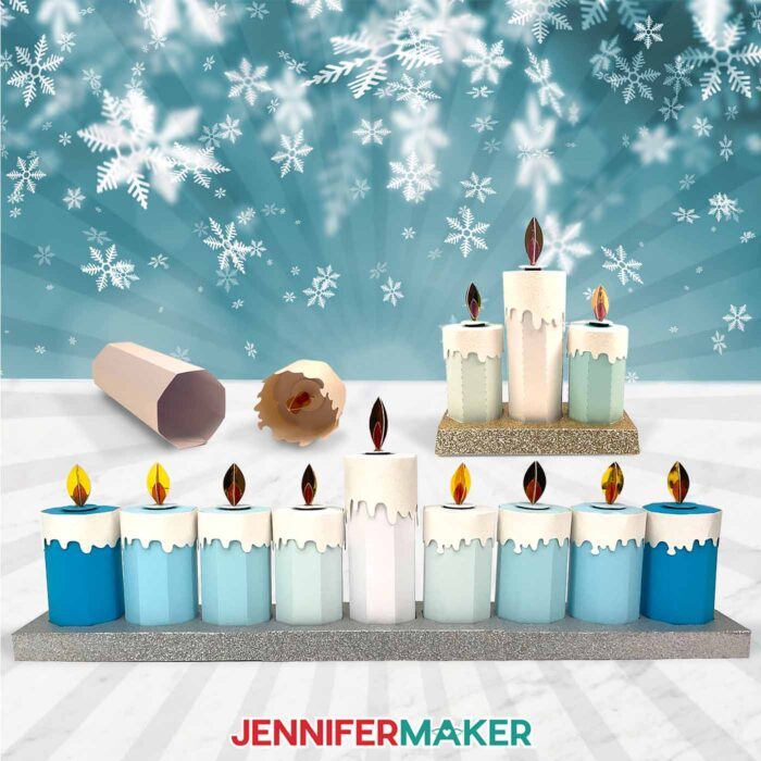 Two sets of Paper Candle Gift Boxes in shades of blue, silver, and white sit on display in front of a snowflake backdrop.
