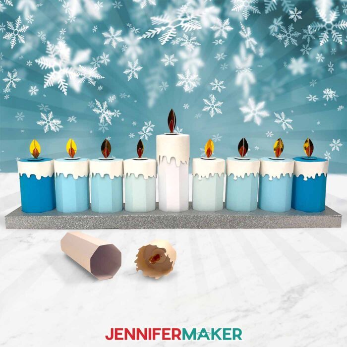 A menorah display of Paper Candle Gift Boxes in shades of silver, blue, and white are displayed against snowflakes and a winter background.
