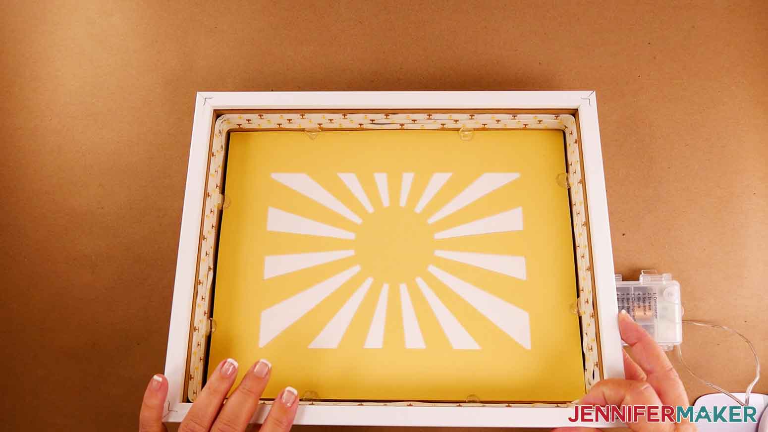 The assembled paper cut light box layers inside the purchased glass shadow box, with glue dots attaching the layer edges to the inside of the frame under the LED strip lights