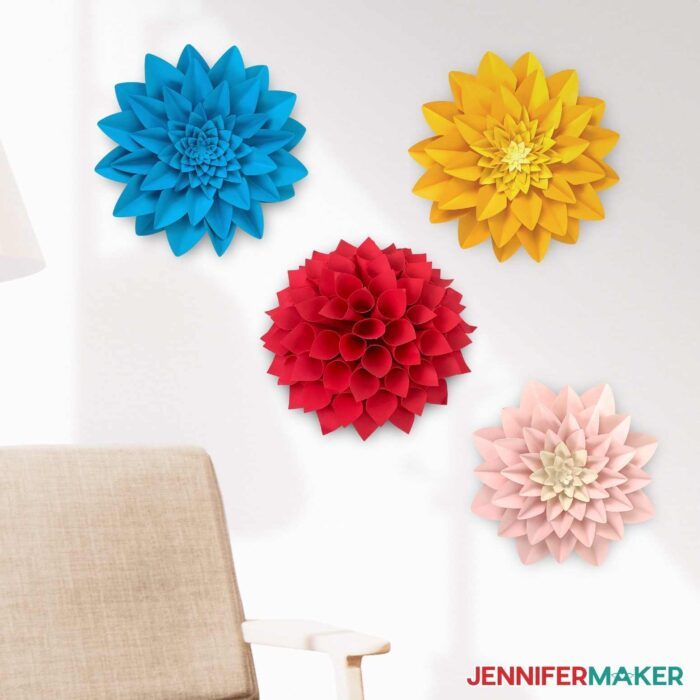 Multicolored paper dahlias hung on a white wall.