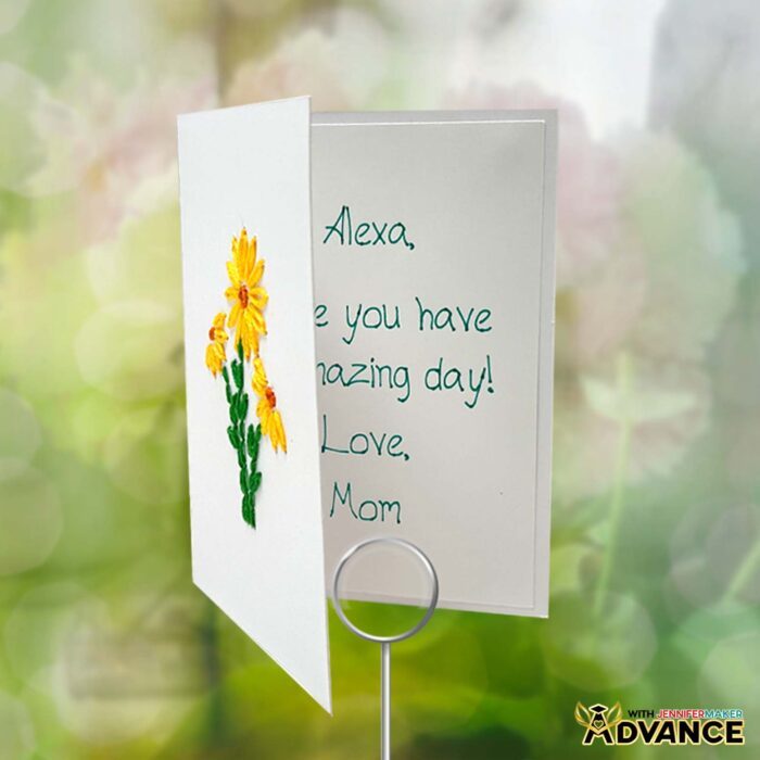 One of the Paper Embroidery Cards with yellow daisies embroidered on the front is partially open to reveal a Cricut-written message inside: "Alexa, Hope you have an amazing day! Love, Mom"