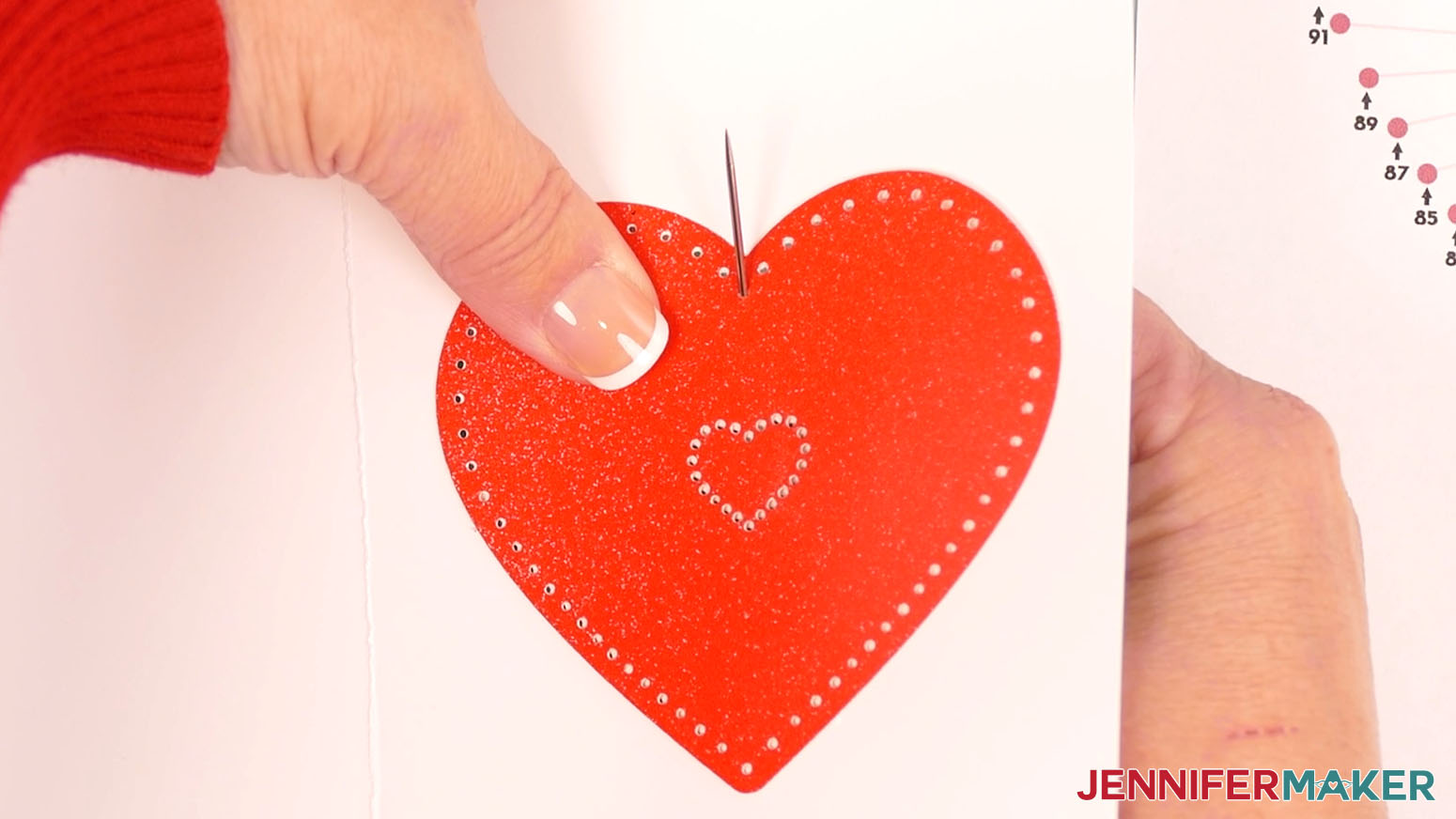 Holding the red heart accent against the white card, bring the needle from behind through hole one.