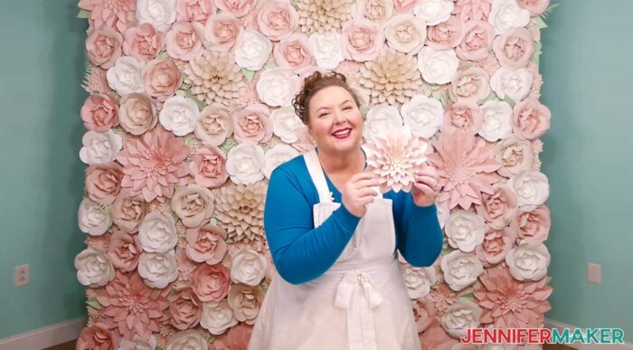 Crafter showing example cardstock flower in front of the completed paper flower backdrop in pinks and greens, large enough for group photos.