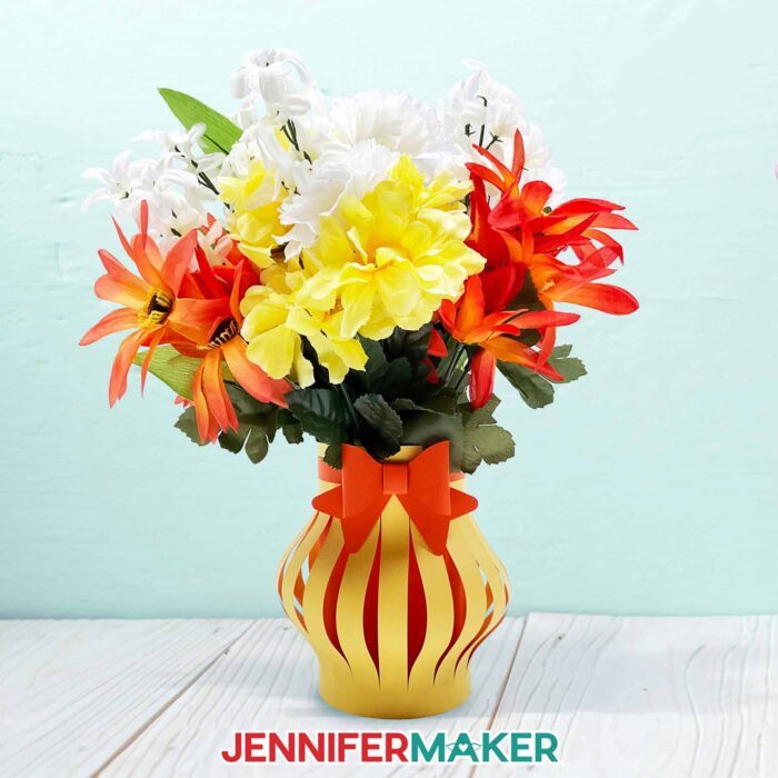 A paper flower bouquet with white, orange, and yellow blooms in a yellow paper vase.