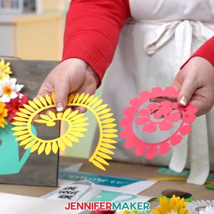 Learn how to create a beautiful paper flower sign with JenniferMaker's tutorial! Jennifer holds un-rolled paper flowers over her work surface.