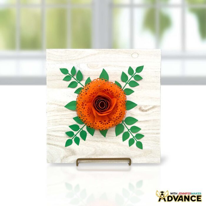 An orange rose paper flower with lace petals sits on a table. Advance custom design by JenniferMaker.