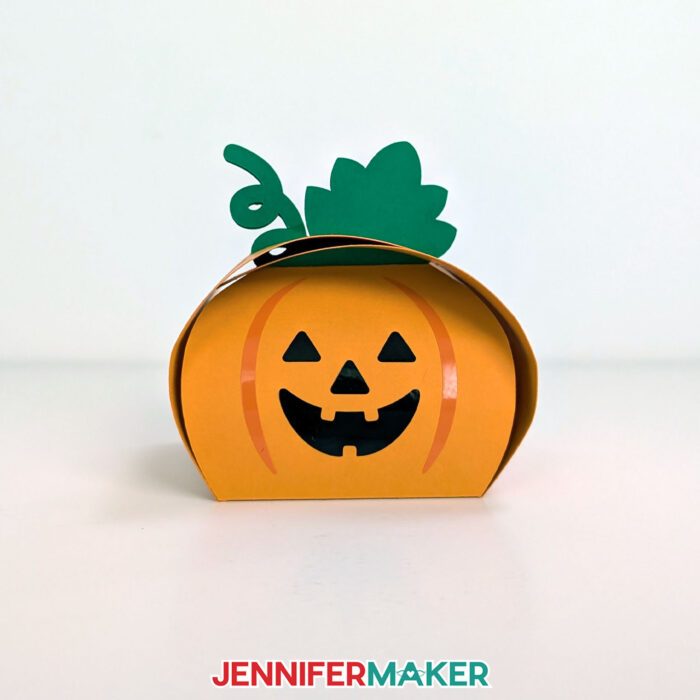 Learn how to make easy Paper Halloween Treat Boxes with JenniferMaker's tutorial! A cardstock and vinyl treat boxes in the shape of a pumpkin sits on display.