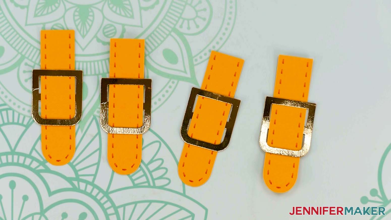 An overhead photo showing four orange handle pieces with pen stitching and gold buckle pieces attached to each one for the paper handbags project
