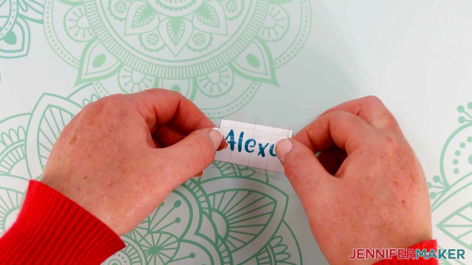 An overhead photo showing two hands using the taco method to apply transfer tape to the Alexa vinyl decal for the keychain of the paper handbags project