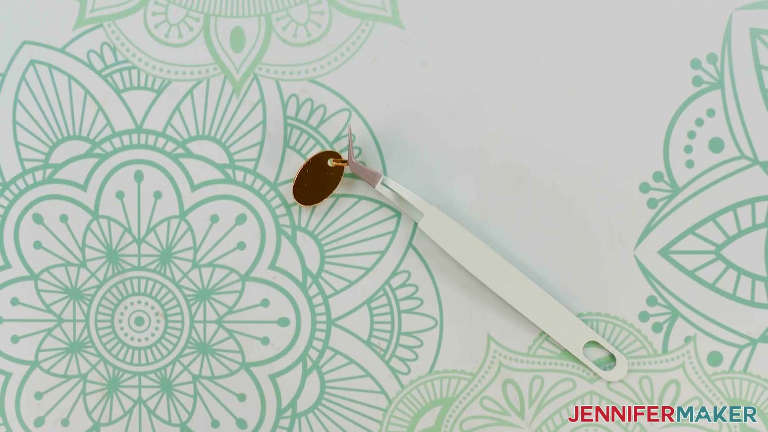 An overhead photo showing Cricut tweezers holding the paper handbags zipper pull attachment piece closed in a loop while the glue dries