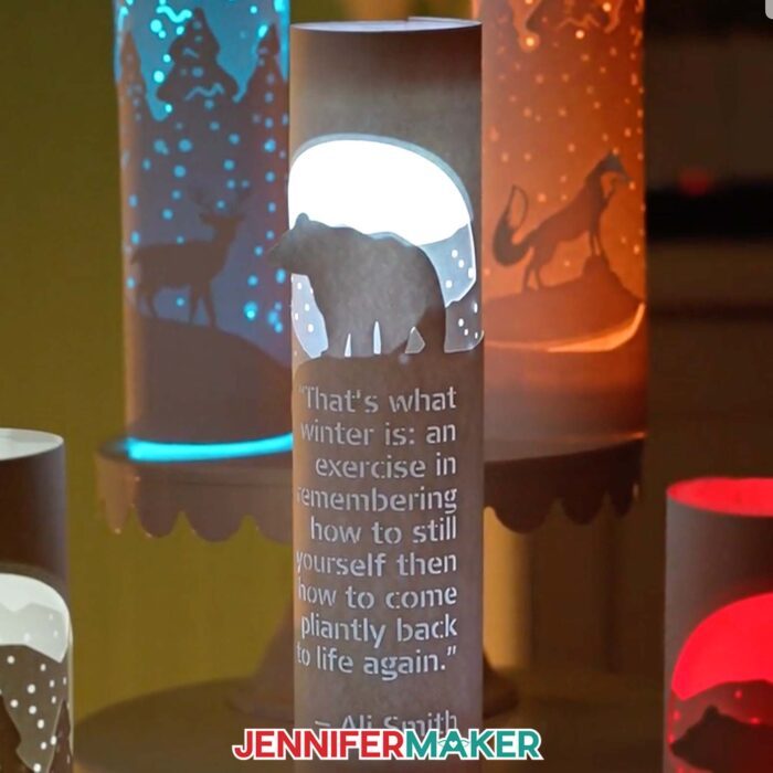 Learn how to make layered paper lanterns with lights with Jennifer Maker's tutorial! An illuminated paper lantern with a bear and custom quote glows in front of two other nature-inspired paper lanterns.