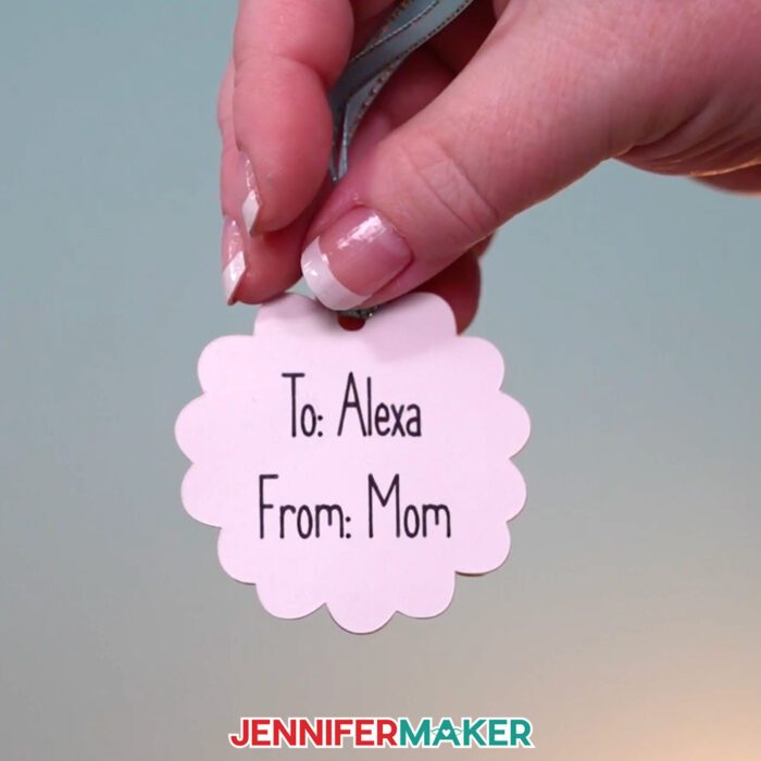 Learn how to make Paper Picnic Baskets with JenniferMaker's tutorial! Jennifer holds a light purple, scalloped-edge gift tag that says "To Alexa, From Mom."