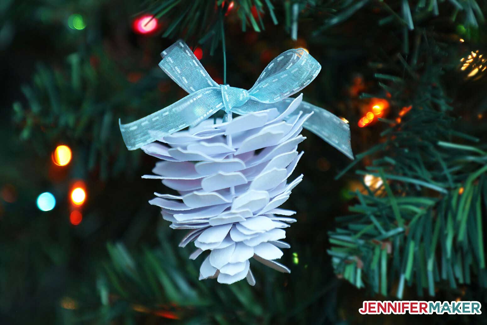 A white paper pine cone hanging from a Christmas tree