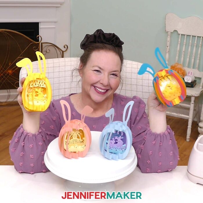 Jennifer Maker sits at her craft table, showing off four Paper Pop Up Easter Egg projects