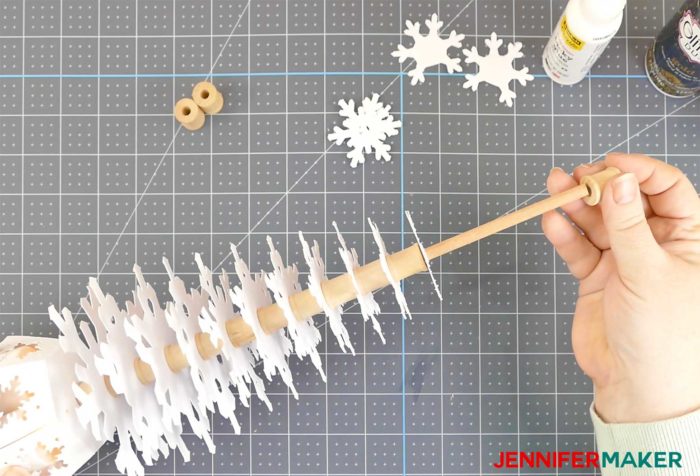 A wooden dowel filled with paper snowflakes and spools to create a paper snowflake Christmas tree