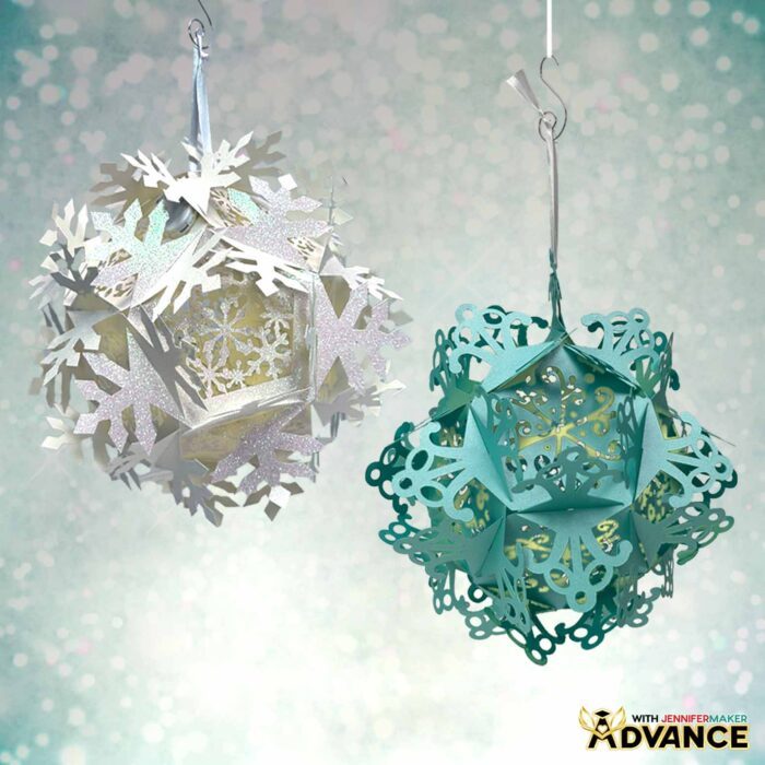A paper Snowflake Lantern cut from white glitter cardstock hangs next to one cut from solid blue cardstock