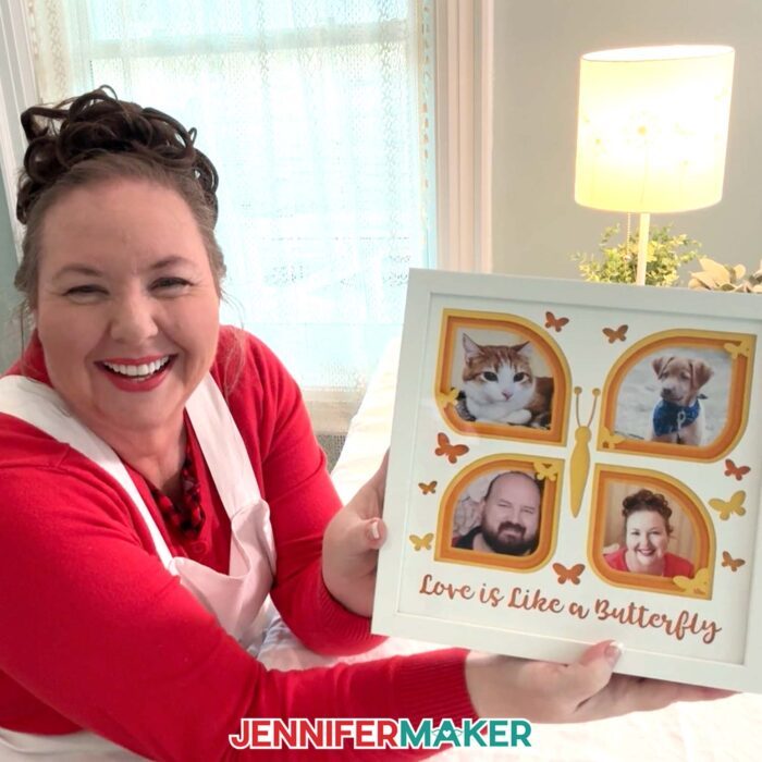 Learn to make a Photo Gallery Shadow Box with layered cardstock in JenniferMaker's tutorial! Jennifer holds up a butterfly-shaped photo gallery shadow box with pictures of her pets, her partner, and herself.