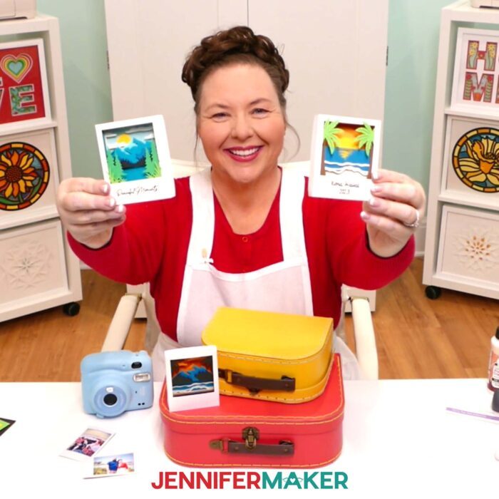 Jennifer Maker holds up two Polaroid Shadow Box projects made of colored cardstock, one of a beach and two of mountains, while sitting at her craft table