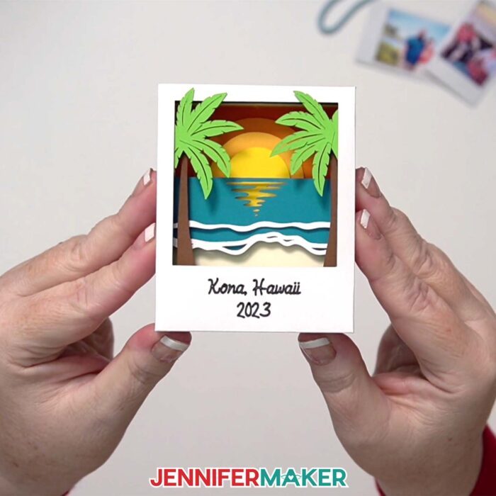 A Polaroid Shadow Box project made of colored cardstock, featuring a beach scene with "Kona, Hawaii 2023" written with Cricut pen at the bottom