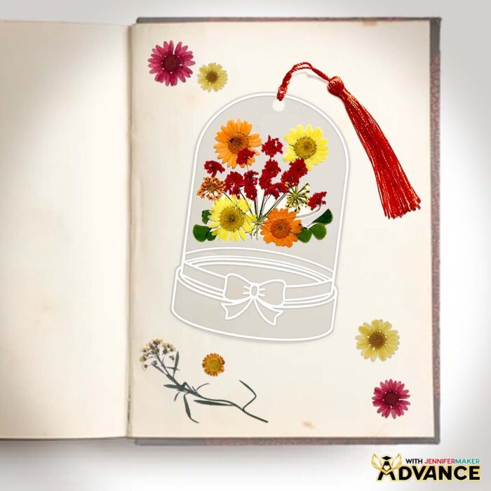 A custom pressed flower bookmark with red, yellow, and orange flowers and a red tassel, made to resemble a glass cloche.