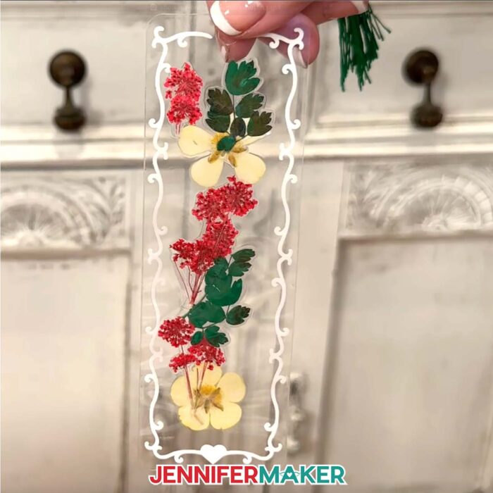 A tall, laminated flower bookmark with red and yellow flowers and green leaves outlined in white vinyl border.