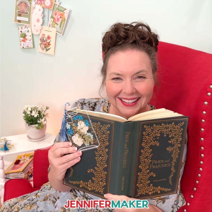 Jennifer sits in a red chair reading "Pride and Prejudice" while holding a pressed flower bookmark with blue and white flowers.