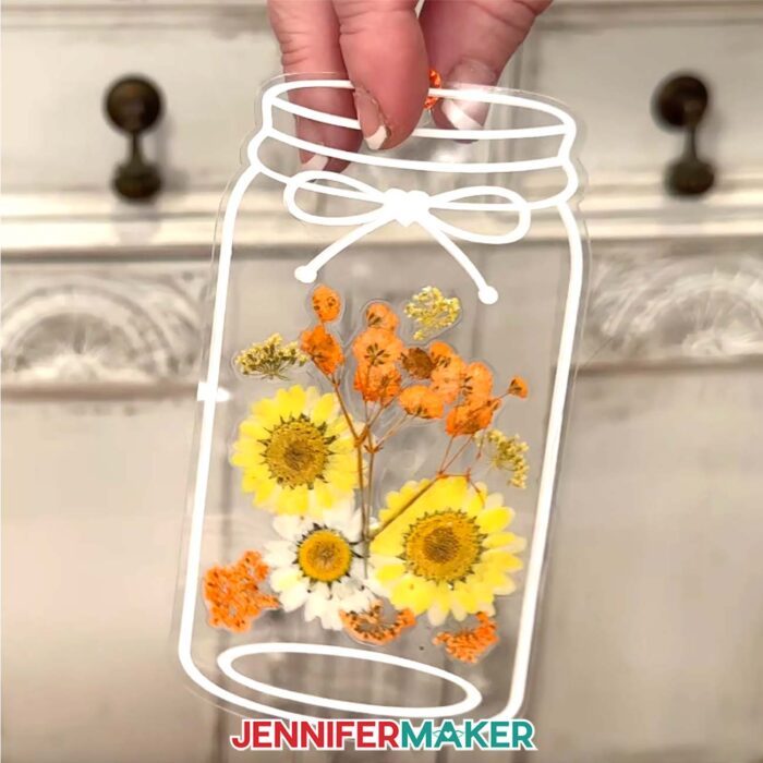 A jar-shaped bookmark with yellow, orange, and white flowers pressed between layers of laminate.