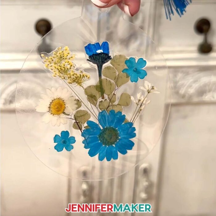 Blue and white flowers pressed inside a flat lamination pouch in the shape of a circle, with a blue tassel attached at the top.