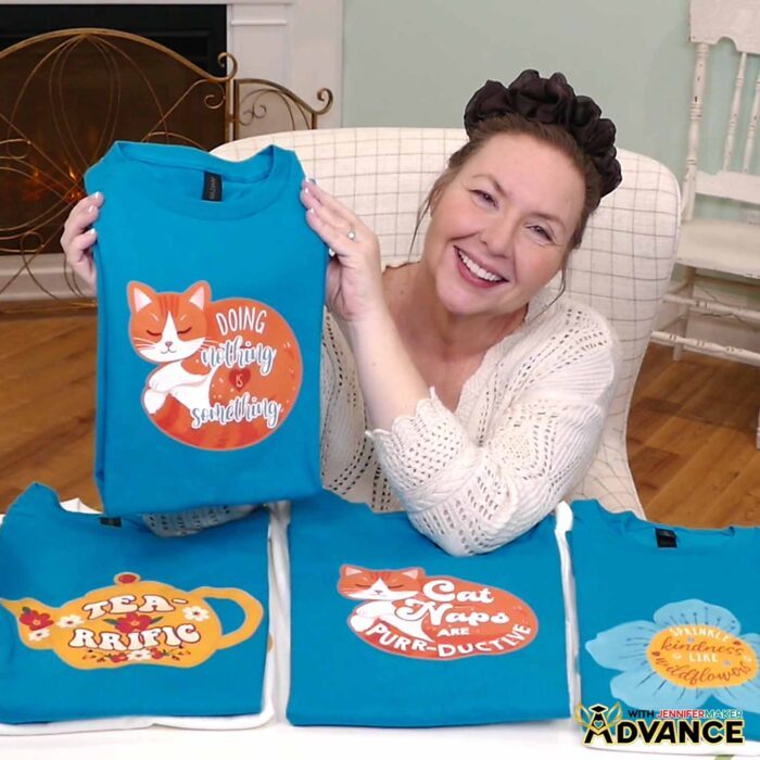 Jennifer Maker shows off a collection of turquoise and white Print Then Cut Iron-On T-shirts on display, featuring cute and cozy designs of cats, teapots, and blooms with quotes