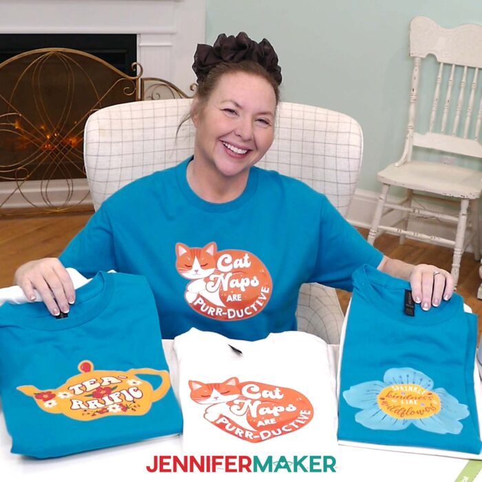 Jennifer Maker shows off a collection of turquoise and white Print Then Cut Iron-On T-shirts on display, featuring cute and cozy designs of cats, teapots, and blooms with quotes
