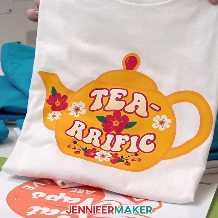 White T-shirt with a Print Then Cut Iron-On design of a teapot with a quote "Tea-Riffic"