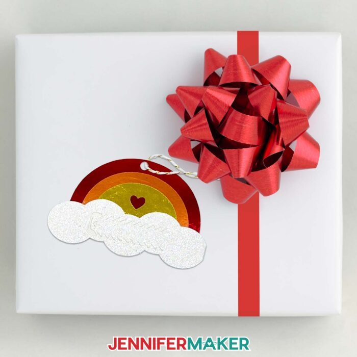 Learn how to make pull tab gift tags with JenniferMaker's tutorial! A rainbow pull tab gift tag hangs from a bow on a wrapped gift.