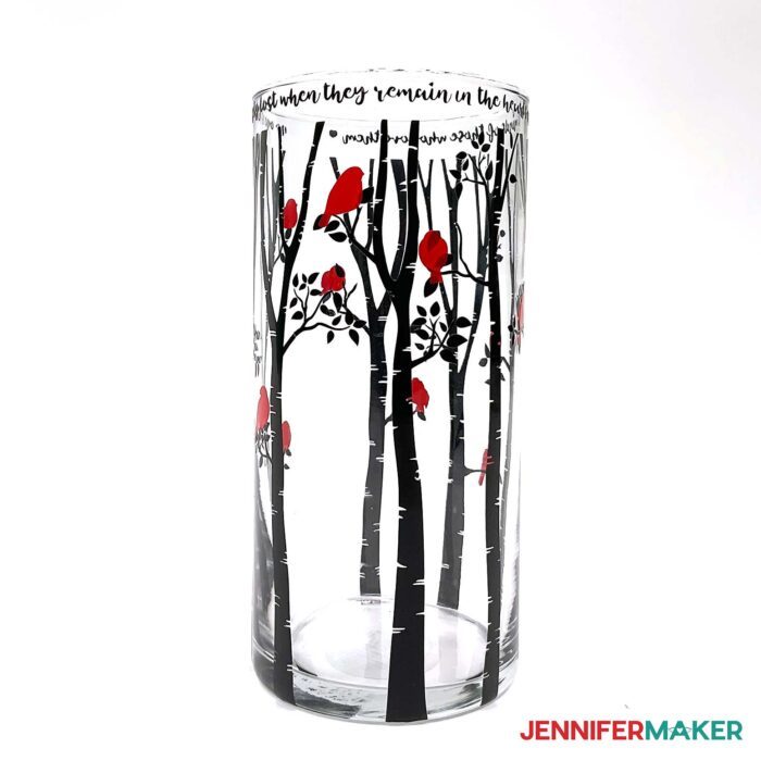 Clear vase with intricate vinyl designs of red cardinals on black trees and a phrase around the top edge. 