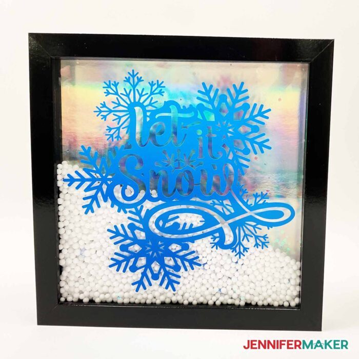 Black shadow box with an intricate vinyl design of snowflakes and Let It Snow in blue on the glass with the inside filled with fake snow.