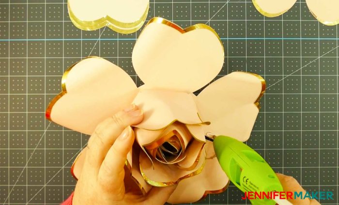 Putting hot glue on paper rose petals to make a giant rose gold paper flower