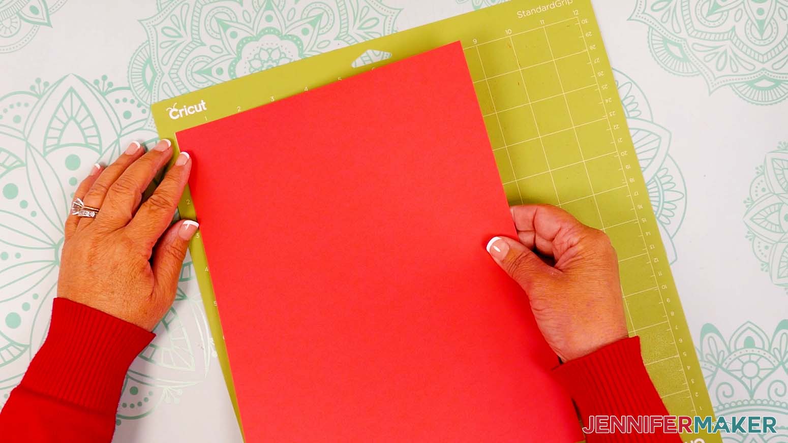A sheet of red cardstock being placed on a green machine mat.