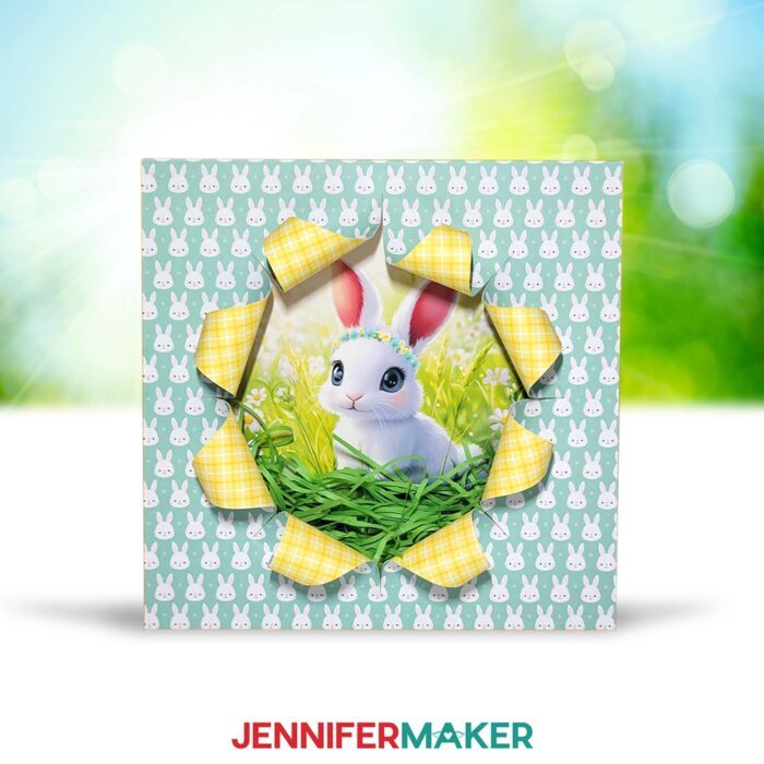 A Spring Busted Canvas project sits outside, covered in patterned spring paper, cut to reveal a cute AI-generated baby bunny image. 