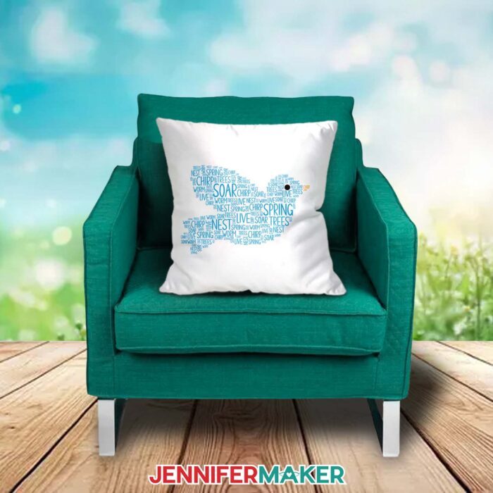 A white pillow decorated with a blue bird-shaped Spring Word Art design filled with spring-related words sits on a green chair outdoors