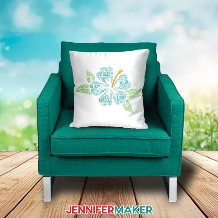 A white pillow decorated with a hibiscus-shaped Spring Word Art design filled with flower-related words sits on a green chair outdoors
