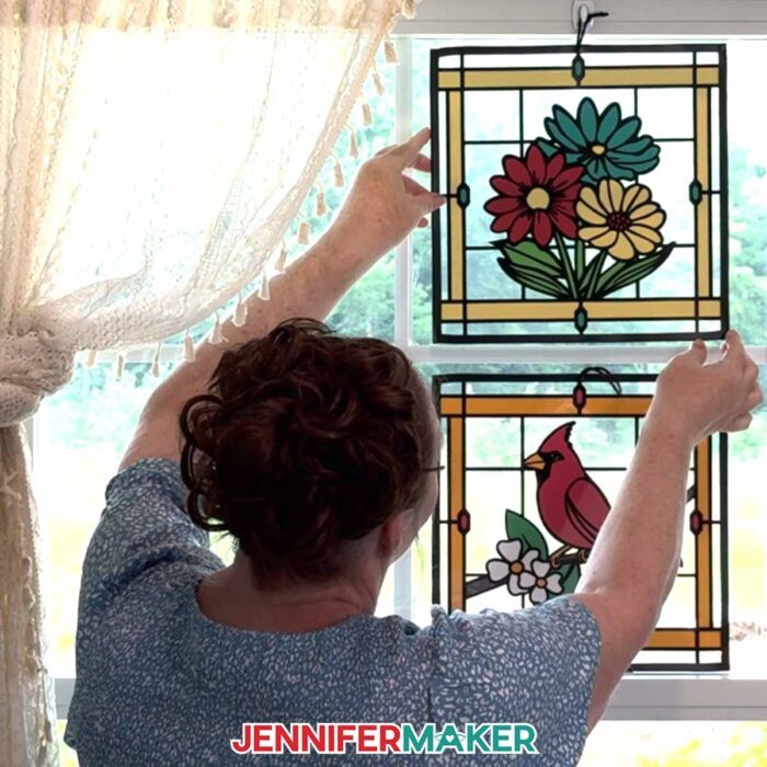 Make Stained Glass Using Paper! Jennifer Maker hangs two paper, acetate, and vinyl stained glass window-inspired craft of flowers and a cardinal in a sunny window